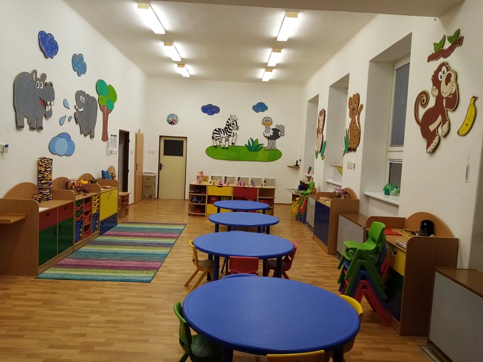 Pohled na přední část třídy s modrými stoly a židlemi a dalším barevným nábytkem vhodným pro pohyb dětí